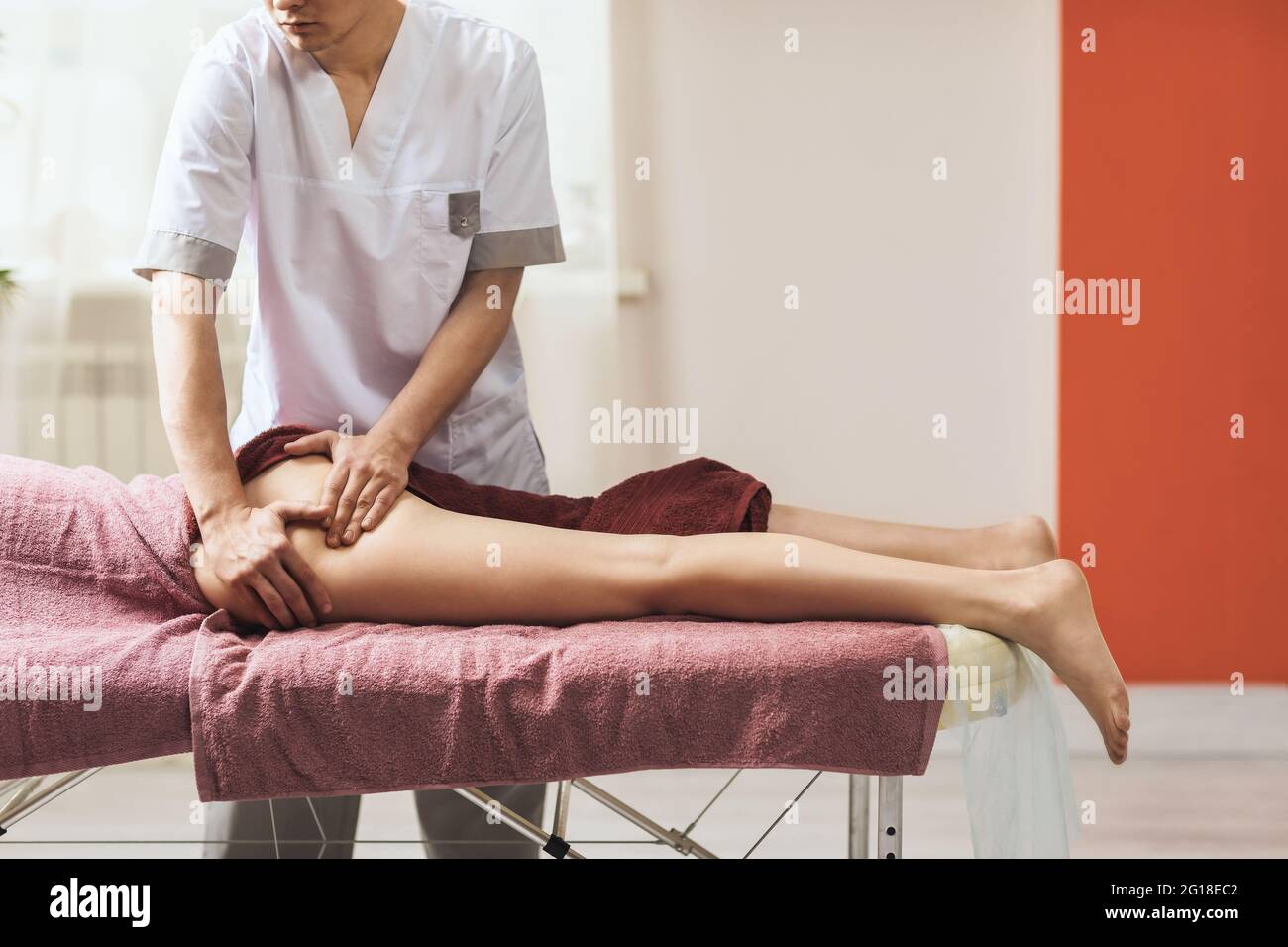 Un hombre que realiza un masaje en el muslo y los músculos glúteos en su oficina. Foto de stock