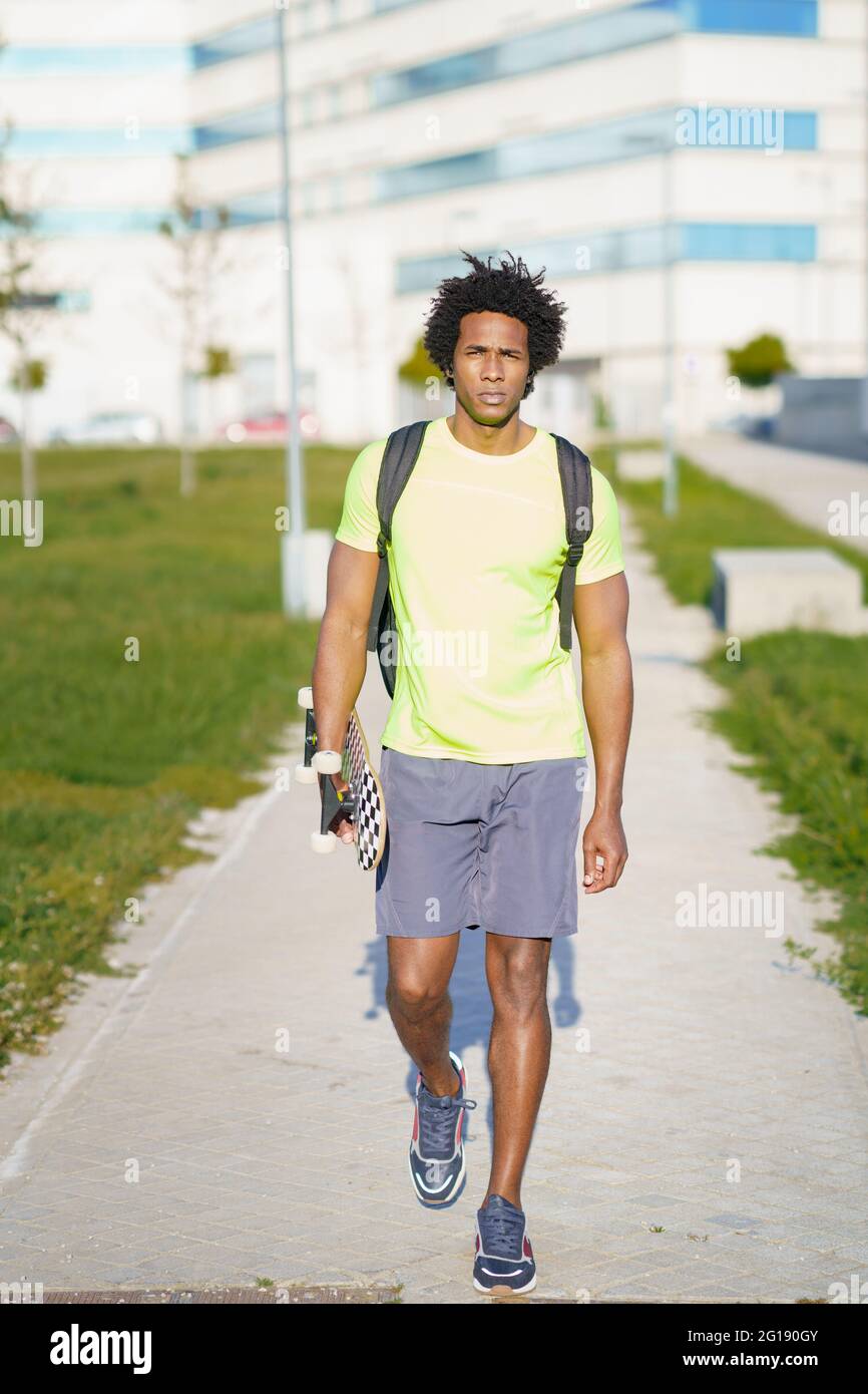 Hombre negro que va para un entrenamiento en ropa deportiva y un skateboard. Foto de stock