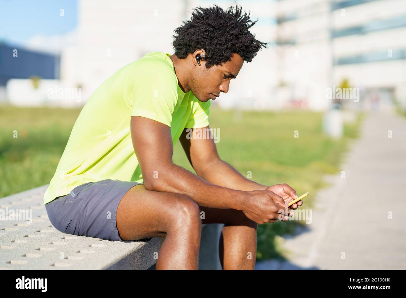 Hombre negro consultando su smartphone con alguna aplicación de ejercicio mientras descansa de su entrenamiento. Foto de stock