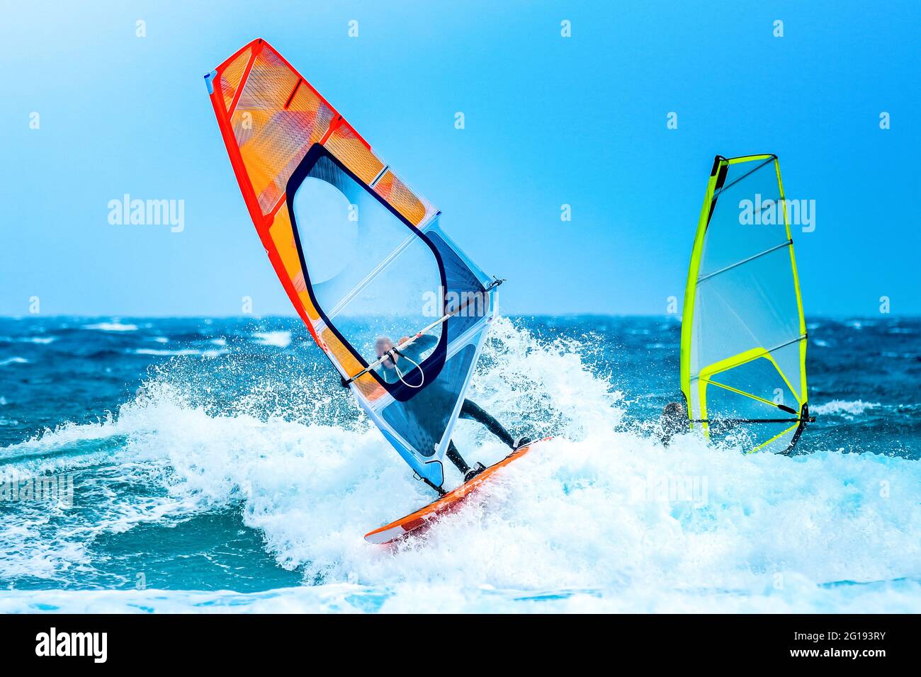 Deportes acuáticos: Windsurfistas montando una ola con una vela naranja en el Océano Atlántico Foto de stock