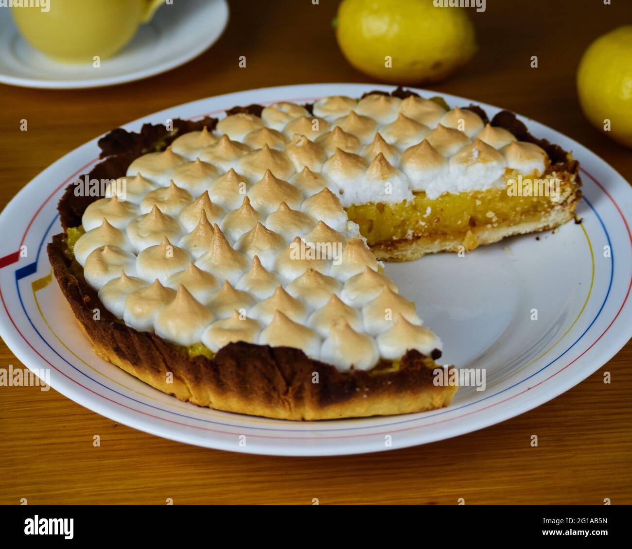 Tarta de limón con merengue sin una rebanada en un plato decorado con dos limones y una taza de café Foto de stock