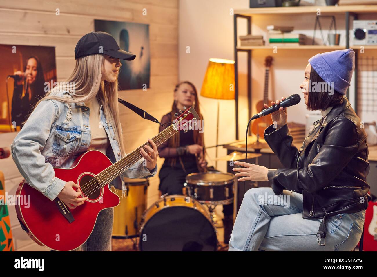 Chica con micrófono cantando entre sus amigos con instrumentos musicales Foto de stock