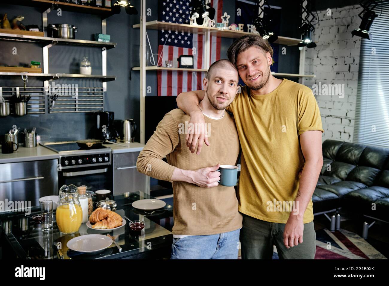 Hombre gay sonriente abrazando a su marido delante de la cámara Foto de stock