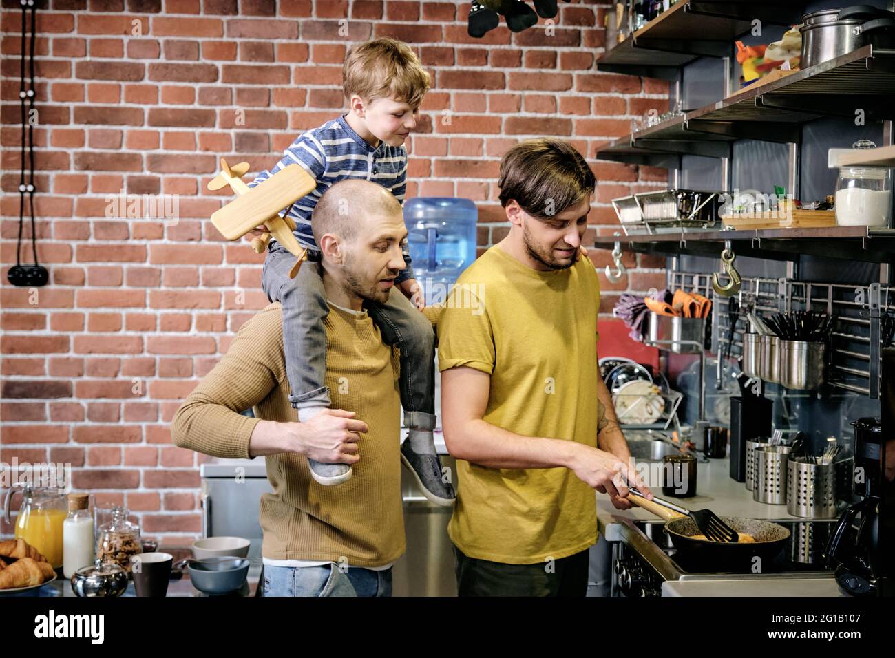 Dos hombres gays felices y un niño pequeño cocinando en el ambiente de la cocina Foto de stock