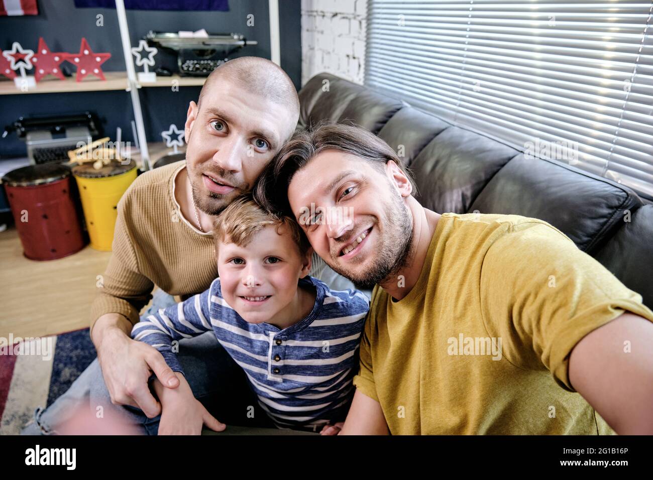 Dos hombres amorosos que hacen selfie con niño pequeño lindo en el ambiente casero Foto de stock