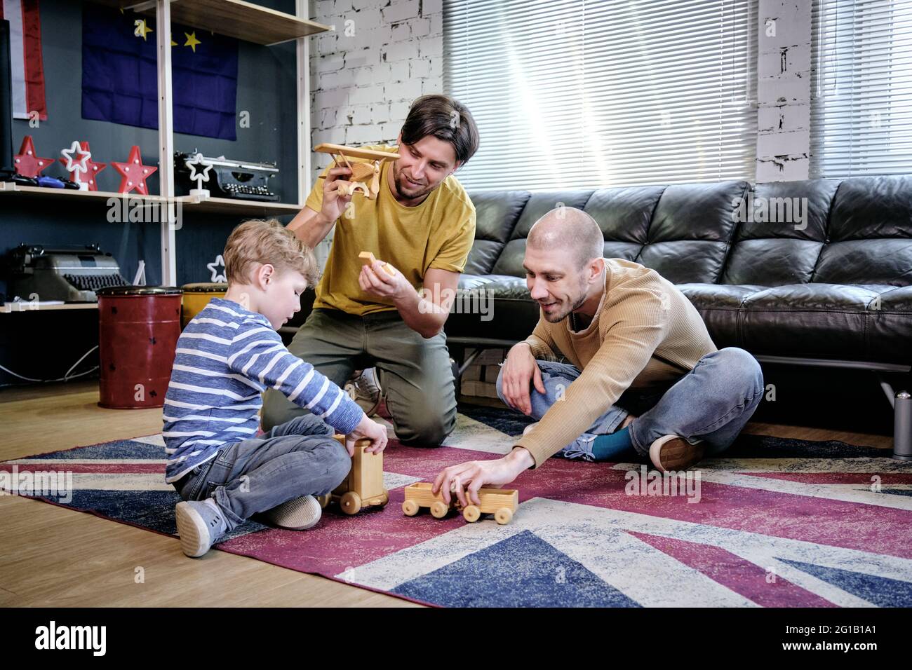 Dos hombres jóvenes y un niño pequeño jugando en el piso de la sala de estar Foto de stock