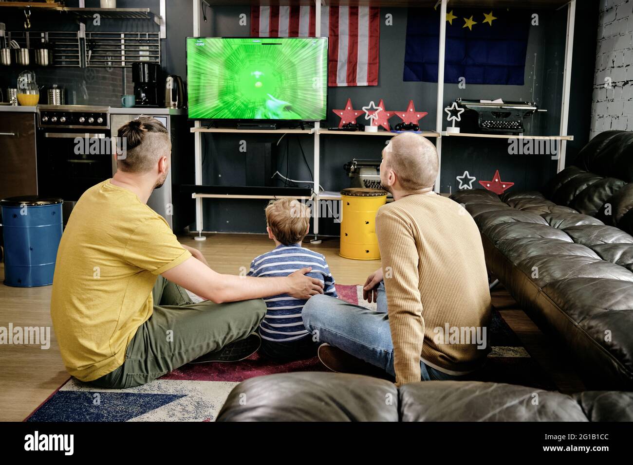 Vista trasera de la familia de tres jugando a videojuegos en la sala de estar Foto de stock