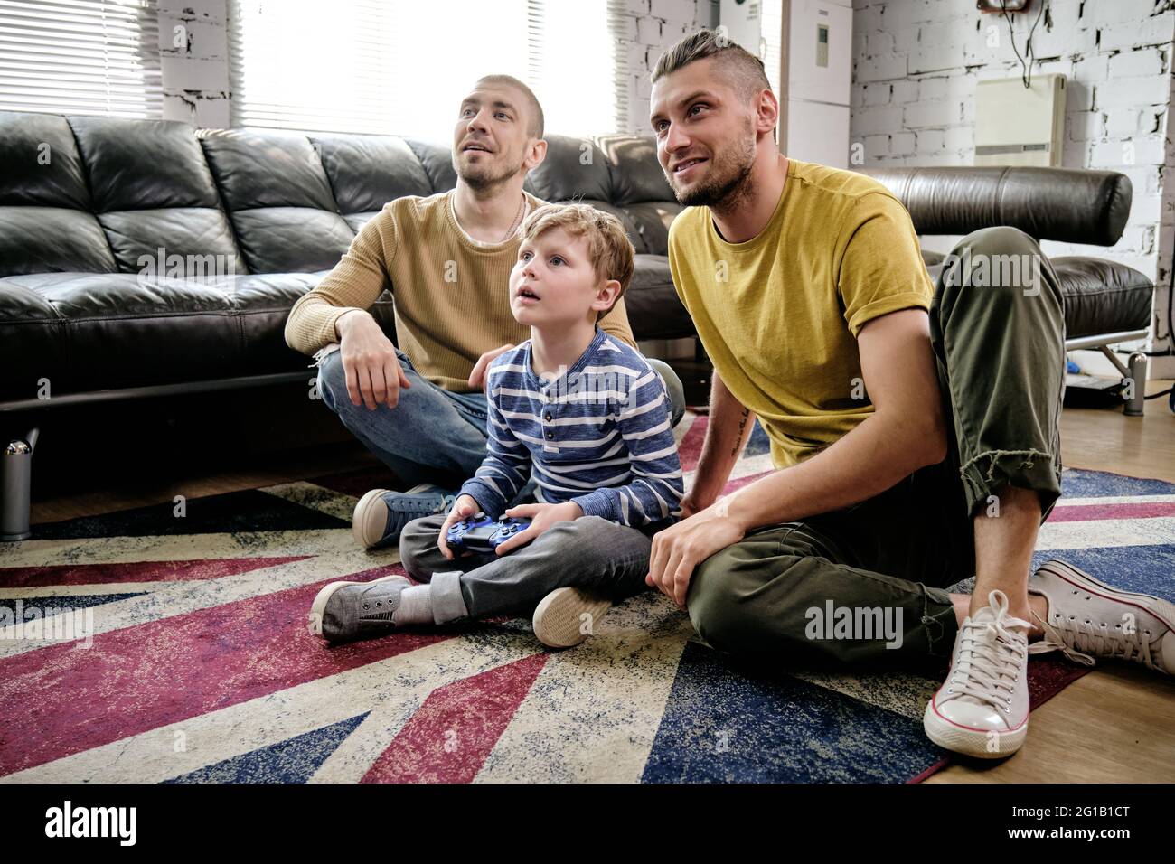 Un chico lindo y dos chicos viendo la televisión mientras estaba sentado en el suelo Foto de stock