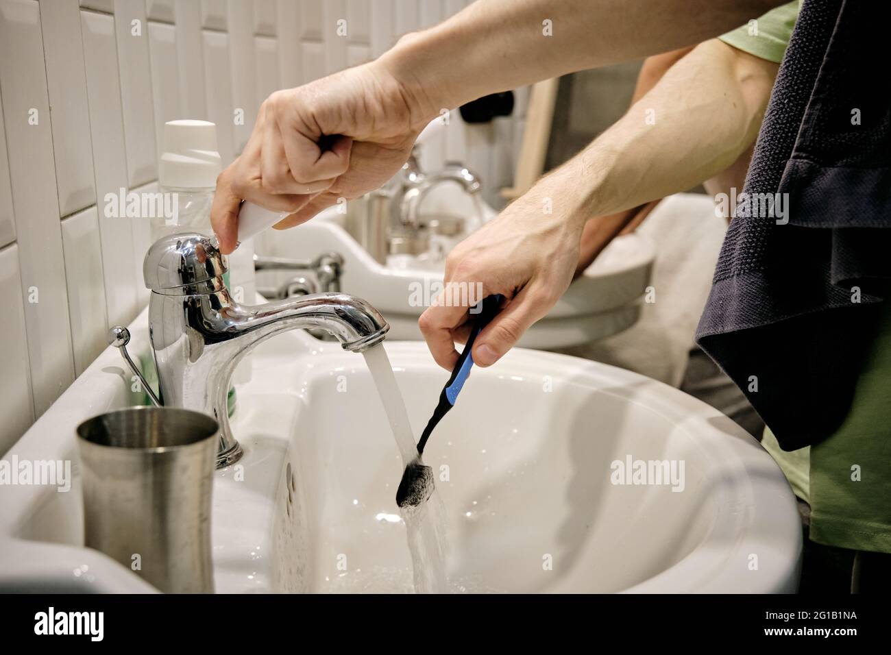 Manos de un hombre joven con cepillo de dientes sobre el lavabo en el baño Foto de stock
