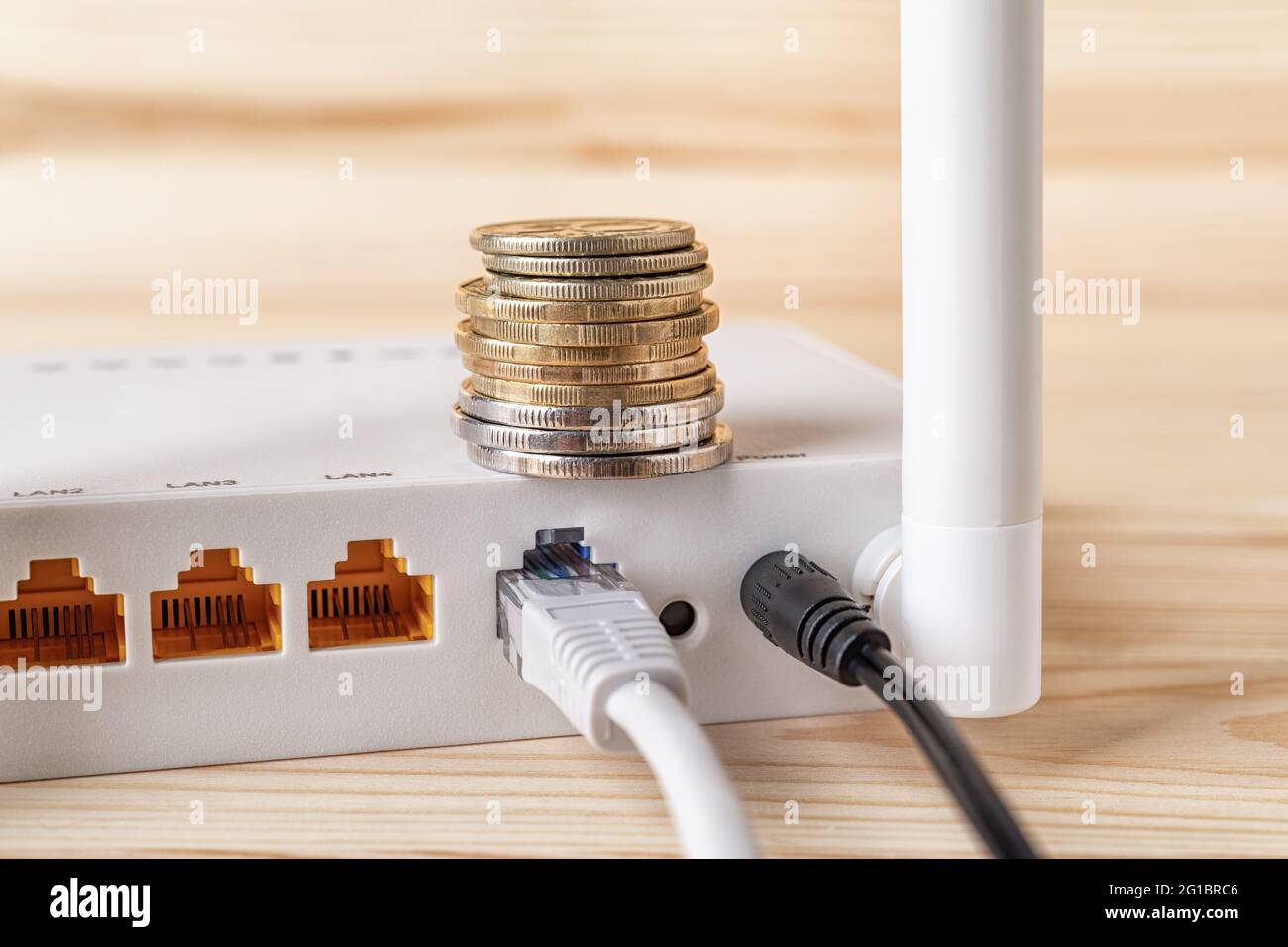 Pila de monedas en el router inalámbrico Wi-Fi blanco con cables conectados  en un escritorio de madera. Pago mensual de Internet, pagar cuentas y ganar  dinero en línea Fotografía de stock -