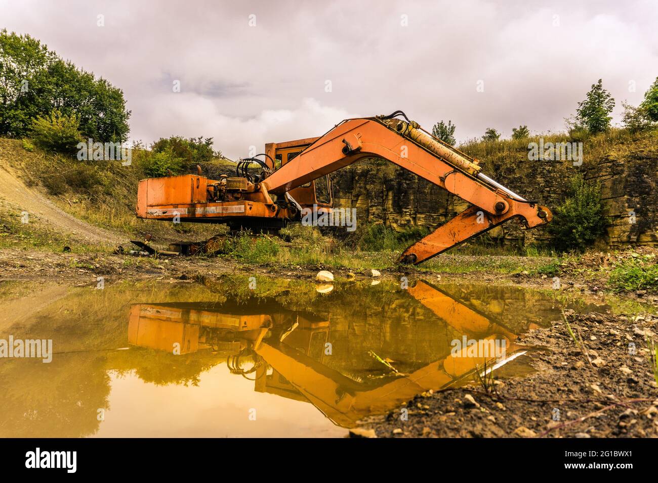 excavadora naranja abandonada que se refleja en el agua fangosa de charco Foto de stock