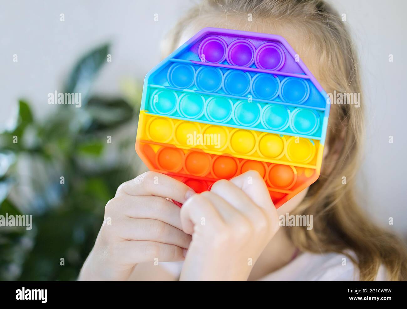 Pequeña niña sosteniendo pop que juguetes, flapping burbuja fidget. Colorido anti estrés sensorial juguete fidget, desarrolla habilidades motoras finas, Foto de stock