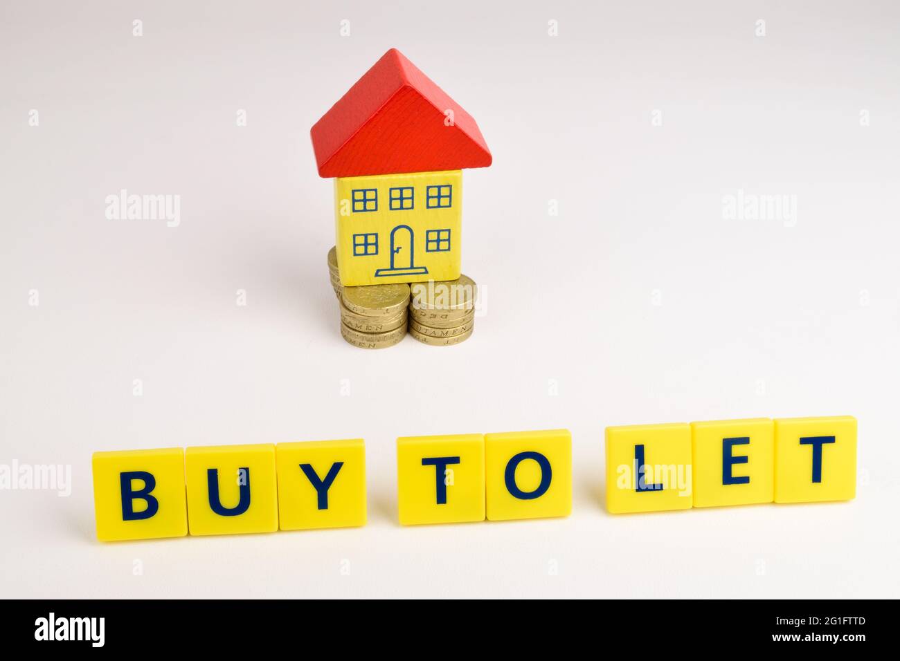 Una casa de juguetes sentada en una pila de monedas con las palabras 'Comprar a Let' delante de ella. Foto de stock