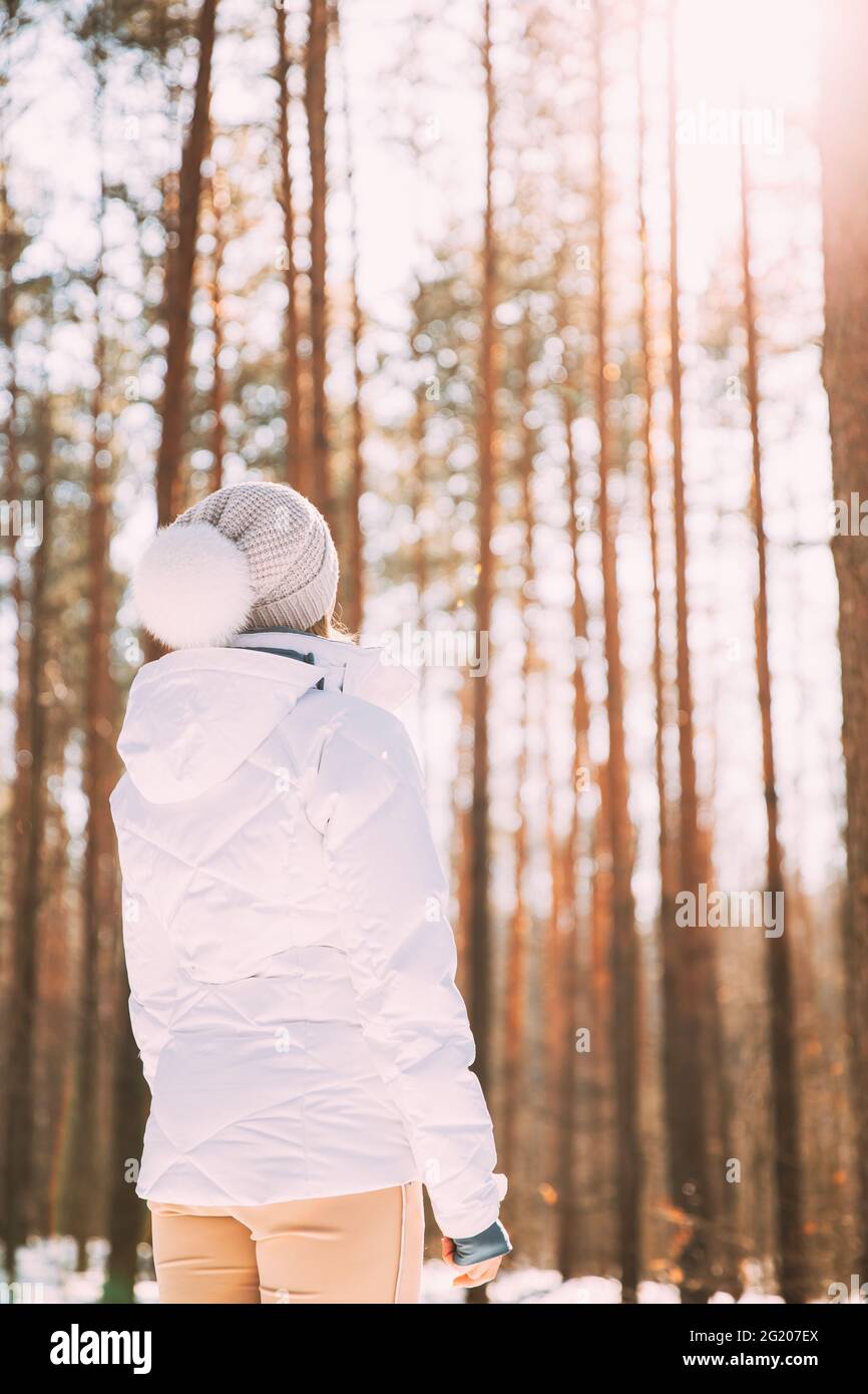 Mujer joven mujer sola de pie en chaqueta blanca y sombrero en el bosque y mirando a la distancia en madera de pino. Vista posterior. Poder de las mujeres Foto de stock