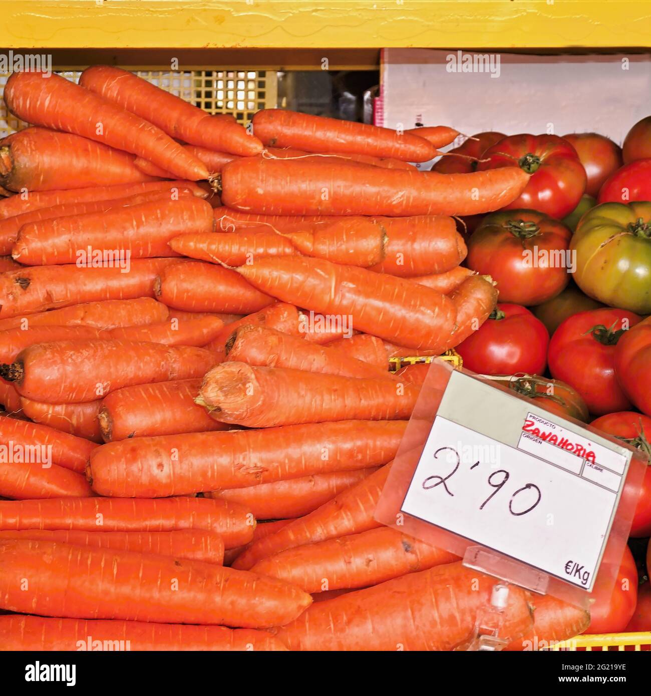 Zanahorias frescas amontonadas una encima de la otra para la venta en un puesto de mercado al aire libre. Al lado hay todavía tomates en verde y rojo. Primer plano en la parte Foto de stock