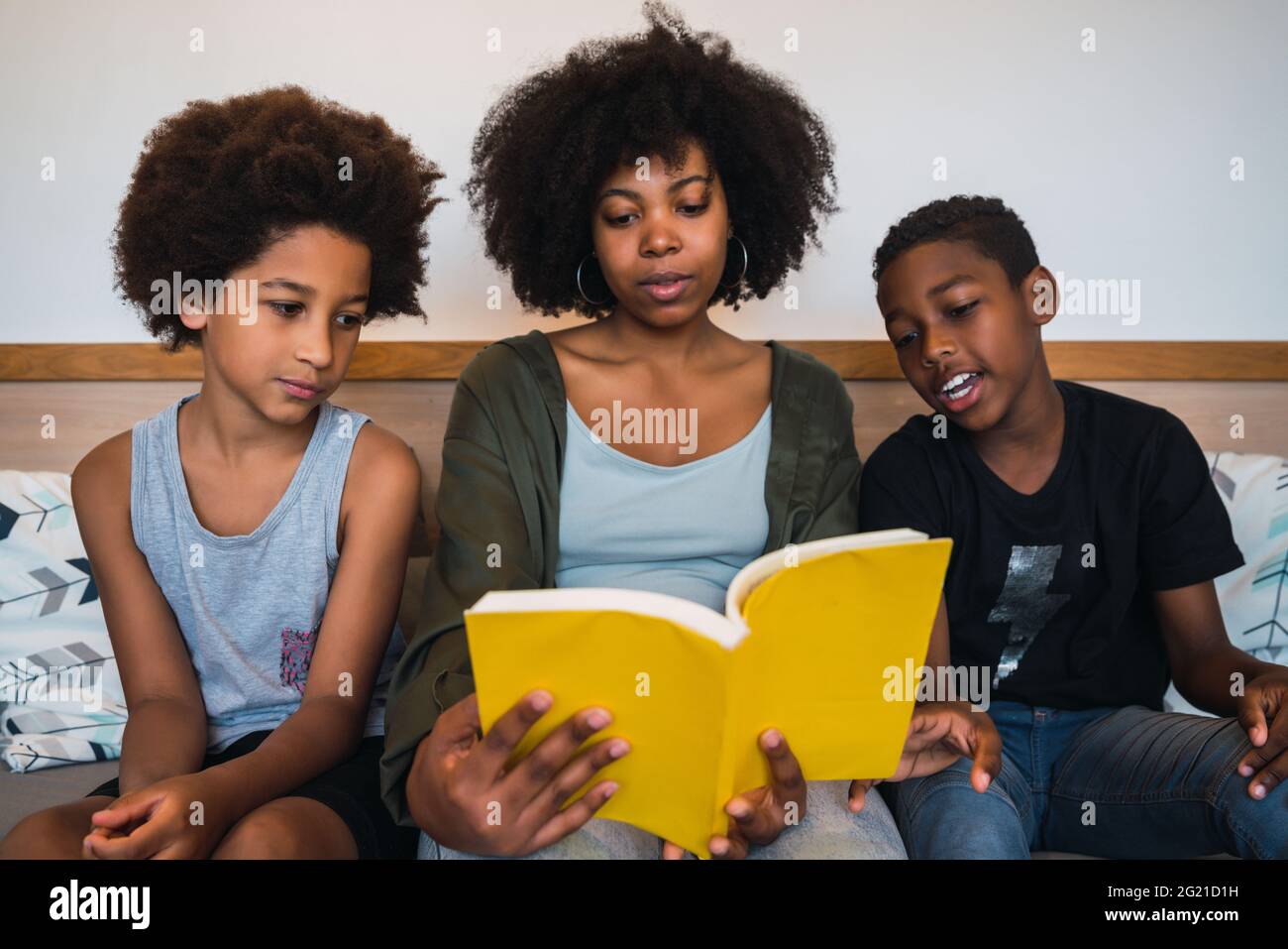 Madre afro leyendo un libro a sus hijos. Foto de stock