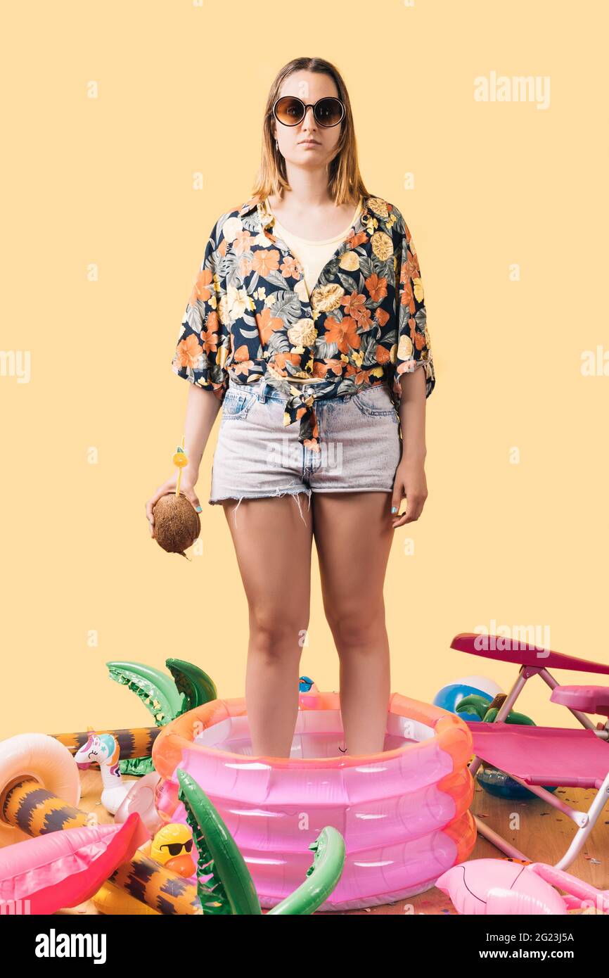mujer desconocida con ropa de verano sosteniendo un cóctel de coco en una  piscina para niños, con muchos inflables en el suelo alrededor de ella.  fiesta en la piscina. vertic Fotografía de