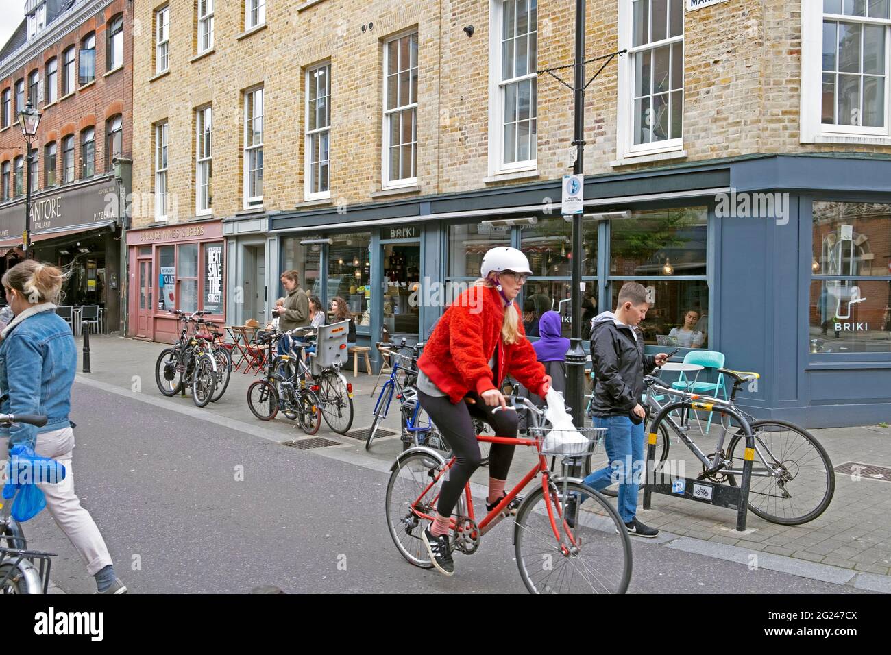 Mujer paseando en bicicleta fuera del restaurante Briki y el cartel de la calle Exmouth Market en el edificio en Clerkenwell Islington Londres EC1 Inglaterra Reino Unido KATHY DEWITT Foto de stock
