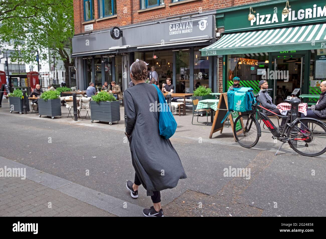 Vista trasera de una mujer caminando por la calle Exmouth Market, fuera de los restaurantes, gente sentada afuera en las mesas en Islington Londres, Reino Unido, KATHY DEWITT Foto de stock