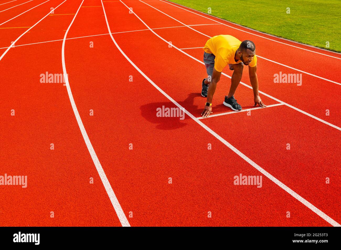 Vista lateral de joven concentrado activo afroamericano hombre sprinter en ropa  deportiva amarilla listo para correr, corriendo en la pista deportiva.  Corredor de atleta Fotografía de stock - Alamy
