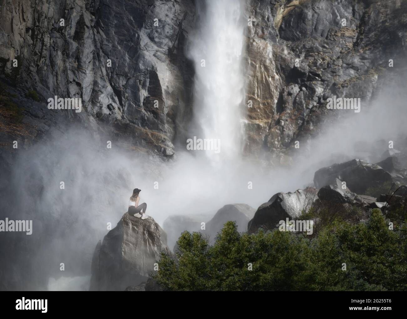 Mujer sentada en una roca en la base de Bridalveil Fall, Parque Nacional Yosemite, California, Estados Unidos Foto de stock