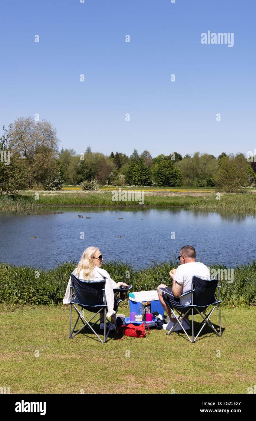 Pareja caucásica de mediana edad sentada en sillas haciendo un picnic junto a un lago, vista trasera, en un día soleado en primavera, Inglaterra Reino Unido Foto de stock
