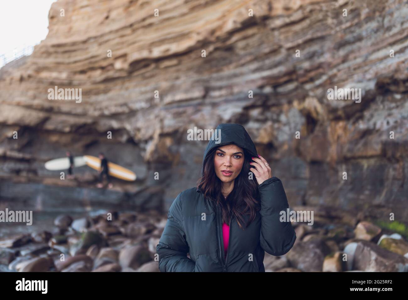 Mujer con sudadera con capucha negra en los acantilados de la playa con  surfistas Fotografía de stock - Alamy
