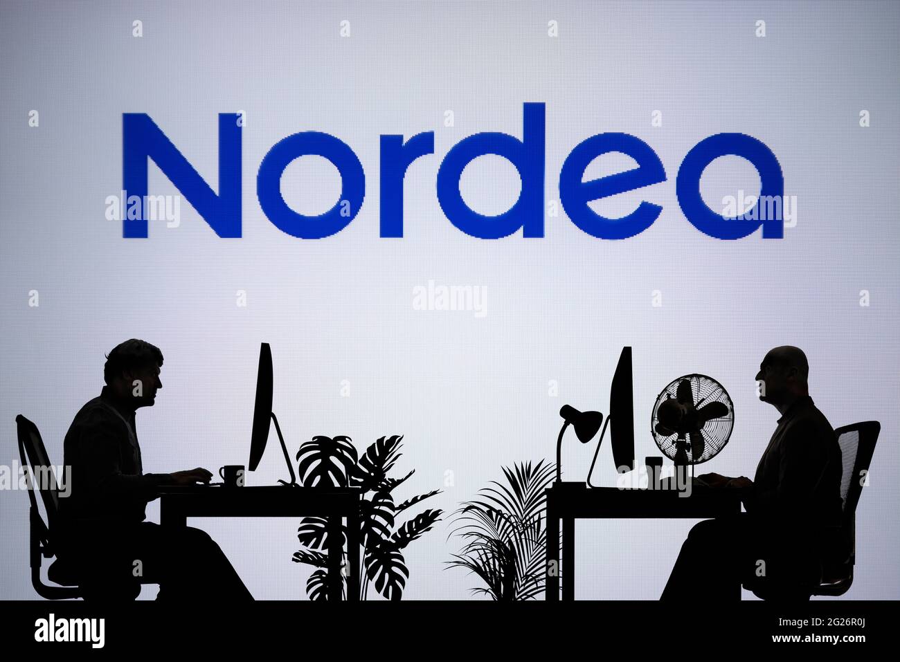 El logotipo de Nordea se ve en una pantalla LED de fondo, mientras que dos personas con siluetas trabajan en un entorno de oficina (sólo para uso editorial) Foto de stock