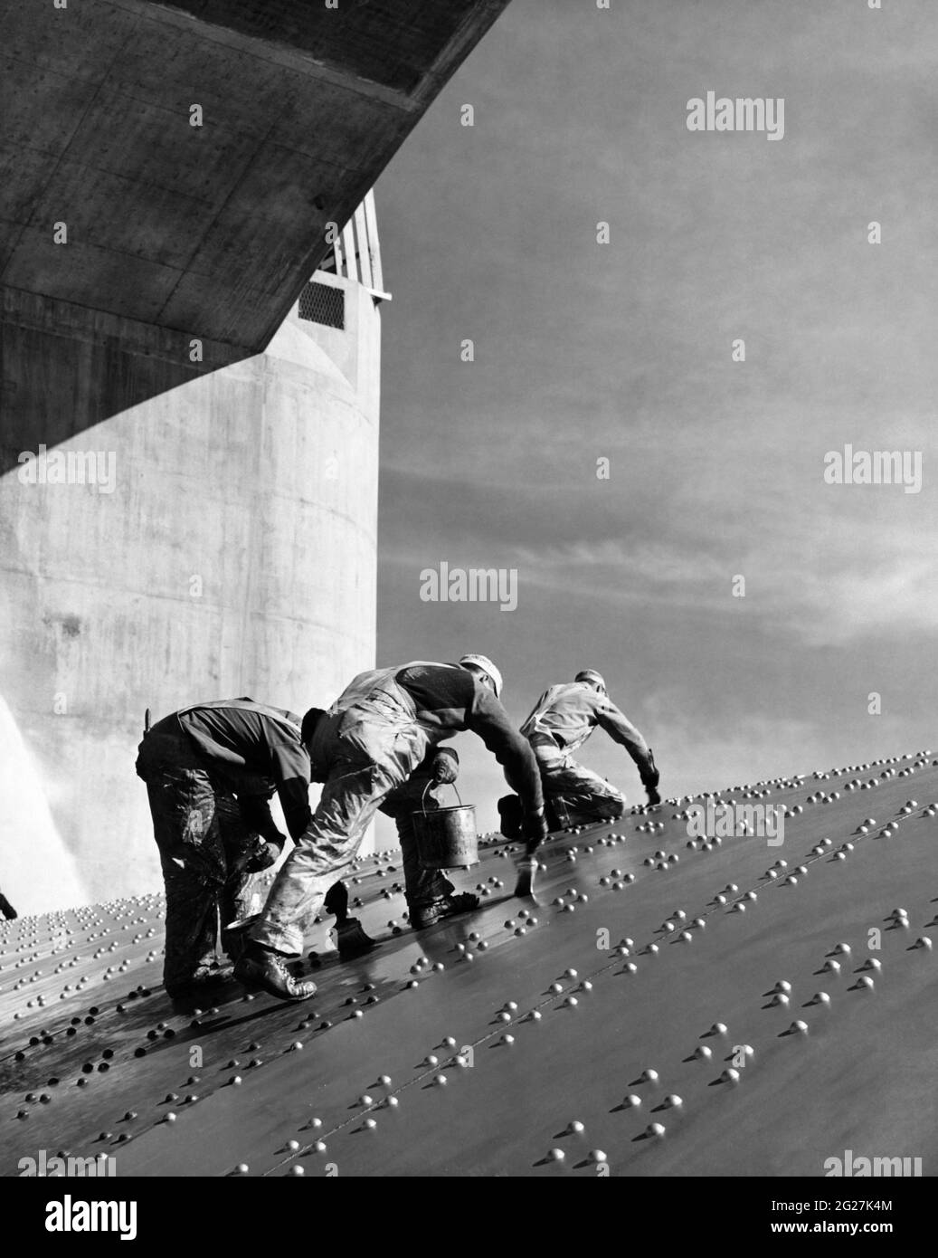 Trabajadores de la construcción que aplican una capa de pintura en placas de acero remachadas inclinadas de la presa Hoover. Foto de stock