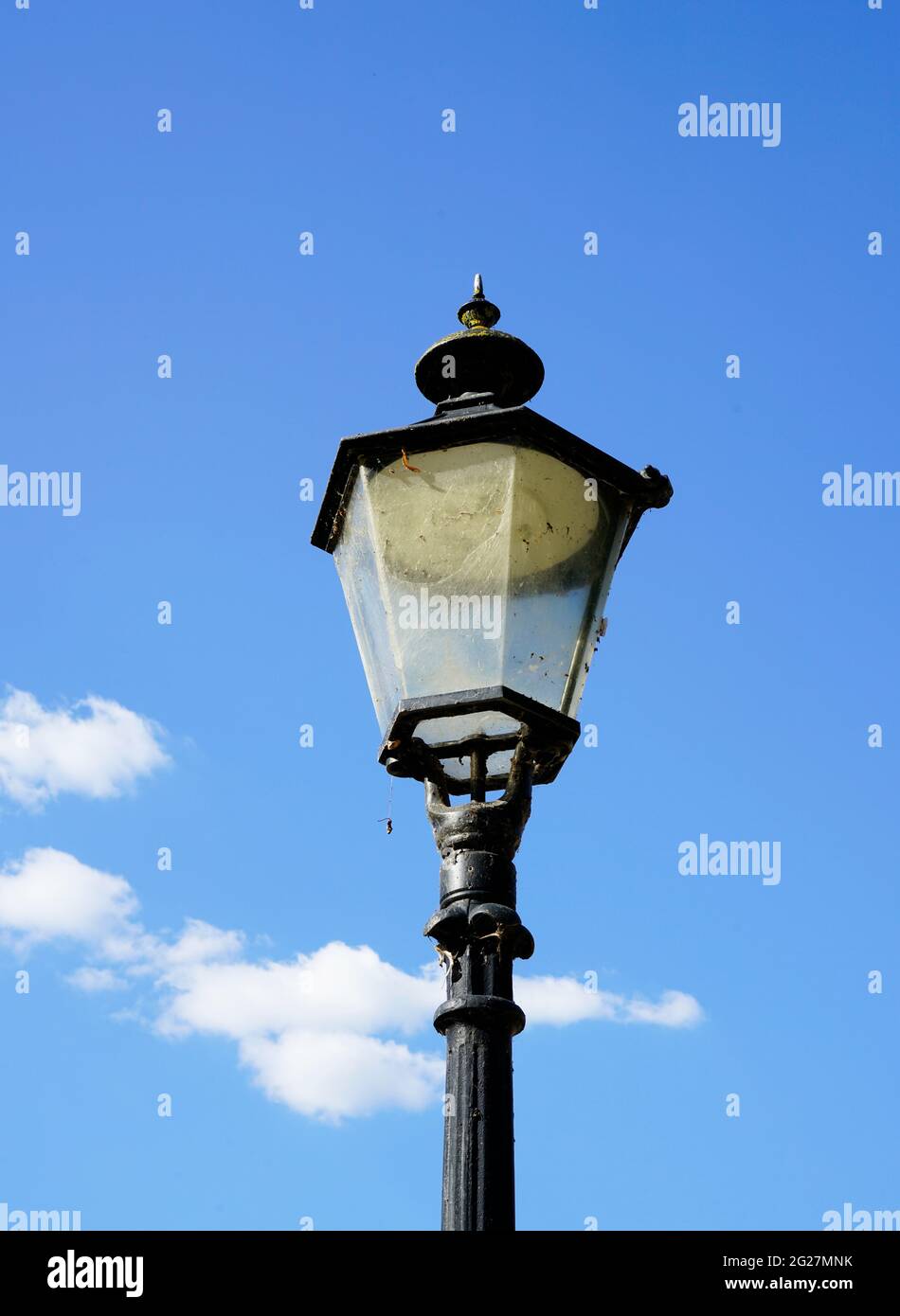 Lámpara de calle vieja de metal negro. Cielo azul con nubes en el fondo. Foto de stock