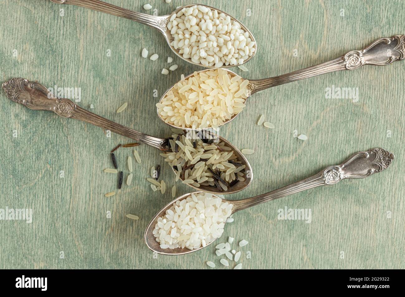 primer plano de diferentes tipos de arroz en cucharas con espacio de copia. Arroz salvaje, arroz sushi, arroz desmenuzado y al vapor sobre un fondo verde de madera Foto de stock