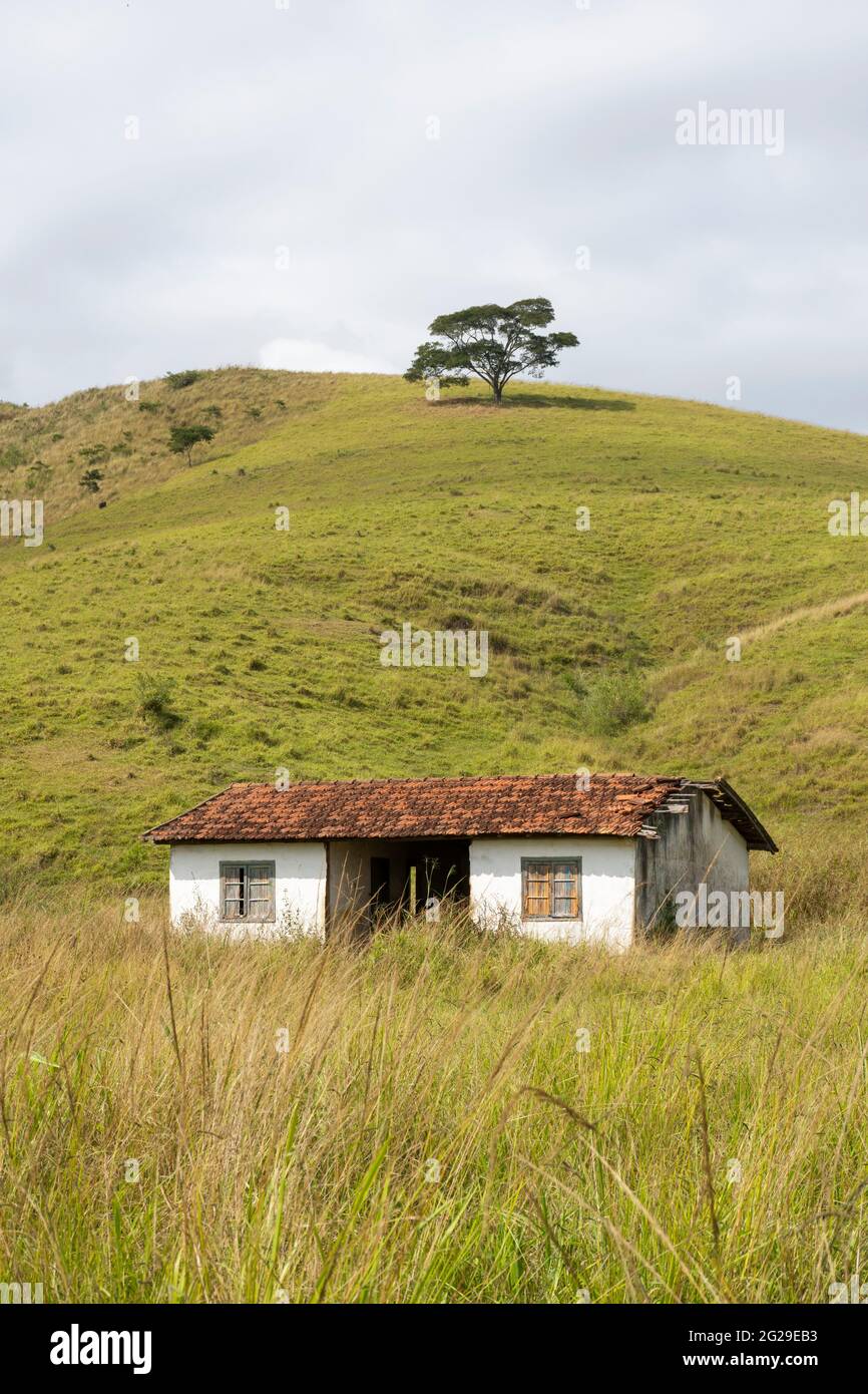 Pequeña casa bajo la colina en tierras de pastoreo en el campo Foto de stock