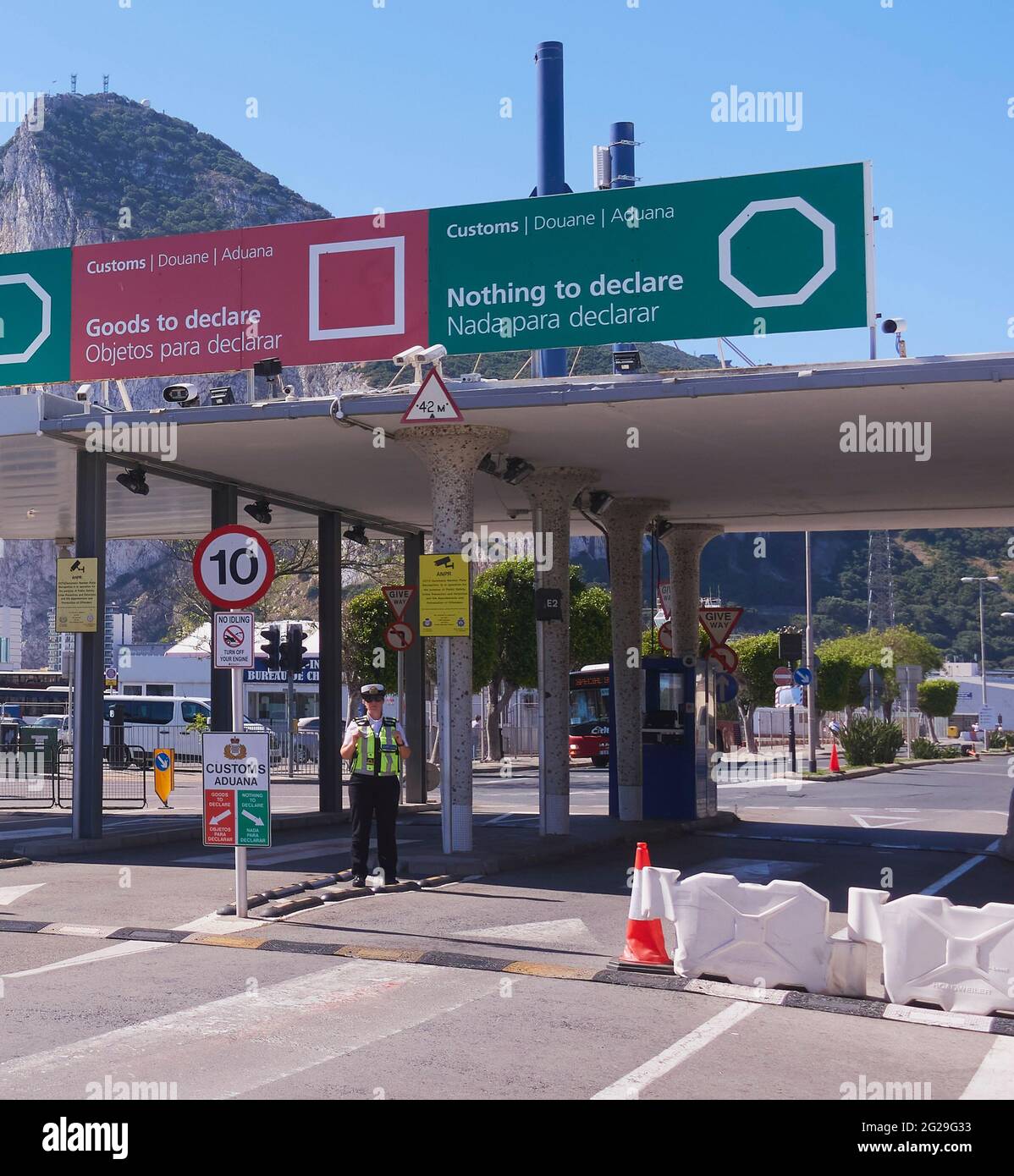 Una mujer solitaria con la Agencia de Fronteras y Guardacostas de Gibraltar se encuentra en una frontera vacía llena de sol bajo las señales de puntos de control aduanero británico Foto de stock