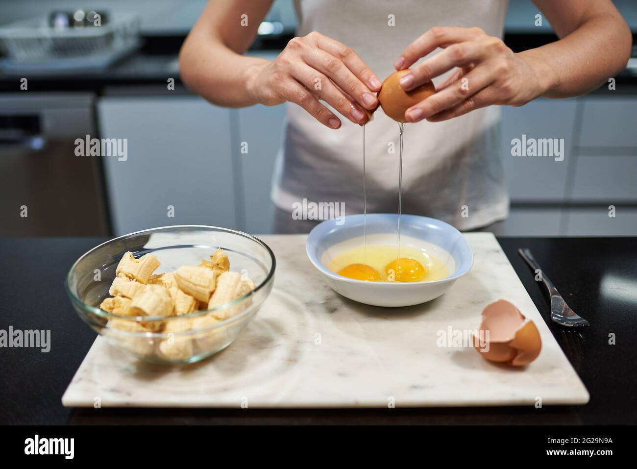 Mujer abriendo un huevo para una receta de tortitas de plátano Foto de stock
