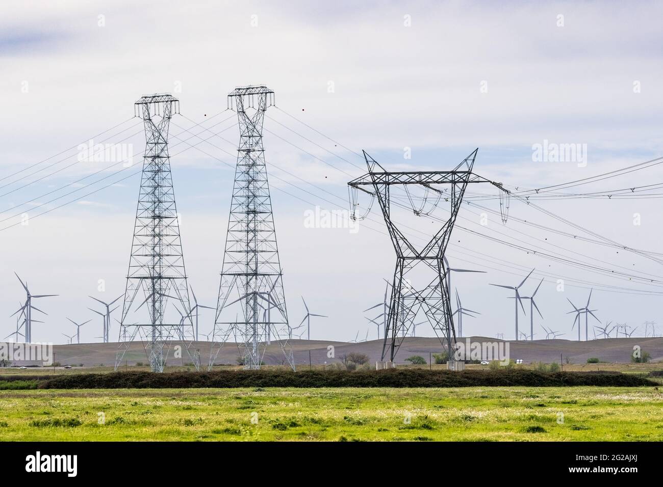 Torres eléctricas de alta tensión y líneas que cruzan el delta de Sacramento-San Joaquín; Aerogeneradores visibles sobre las colinas en el fondo; Solano Foto de stock