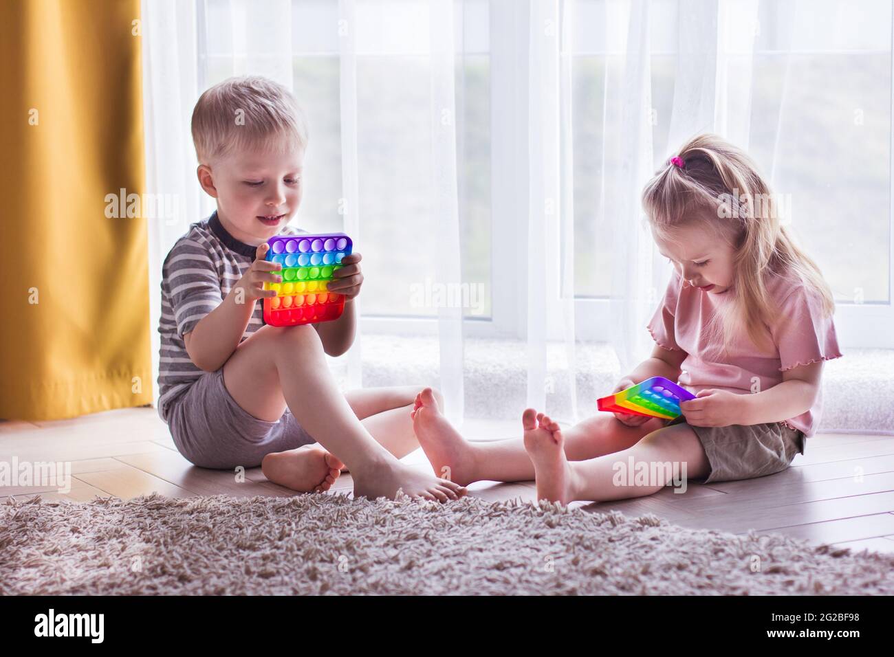 Niño y niña niños juegan con el juguete pop it. Juego de moda para niños y adultos estresados. Juguetes de burbuja y esquisados. Kid p Fotografía de stock -