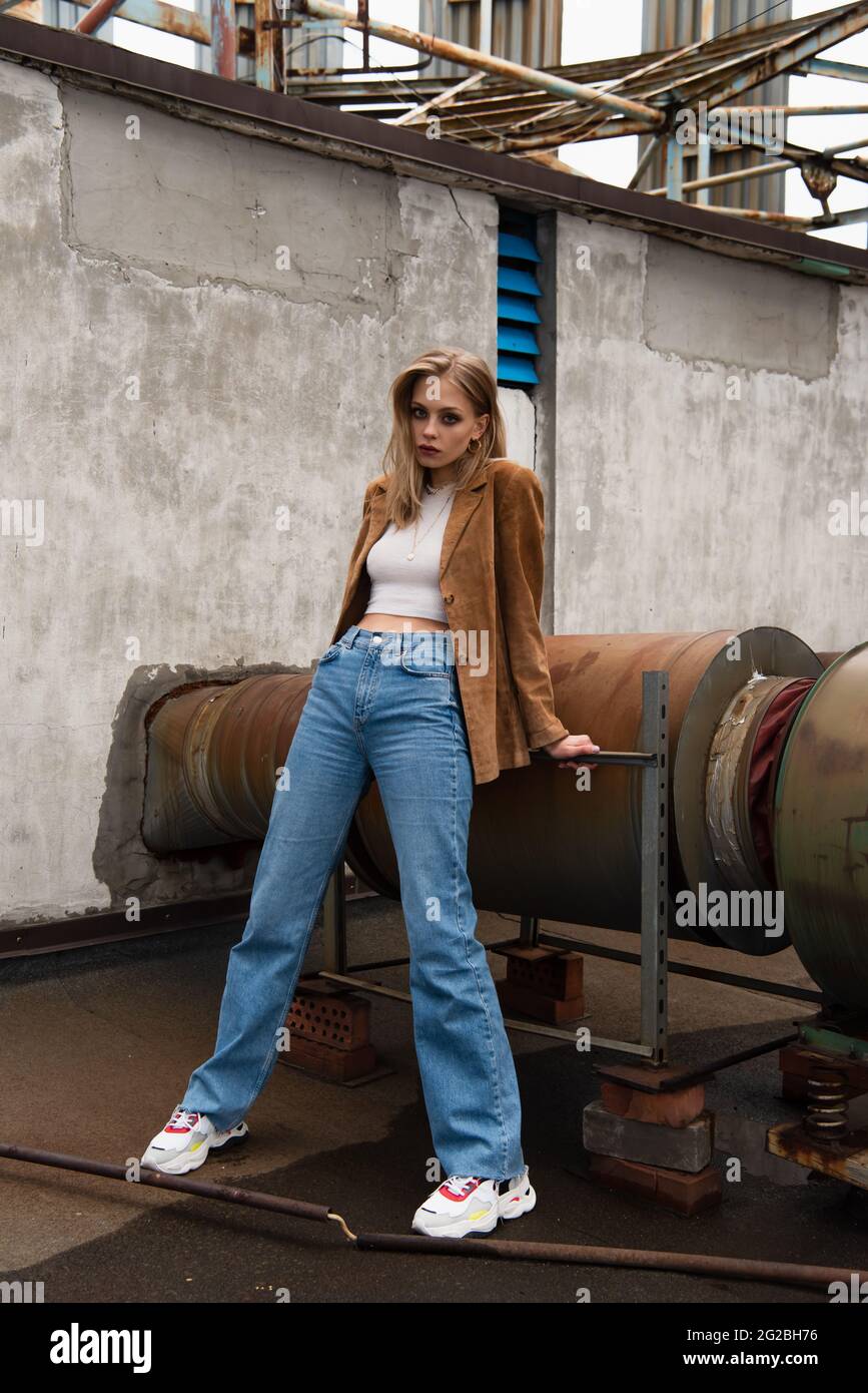 mujer rubia a lo largo de toda la prenda con jeans, blazer de ante y  modernas sneakers posadas en el tejado Fotografía de stock - Alamy