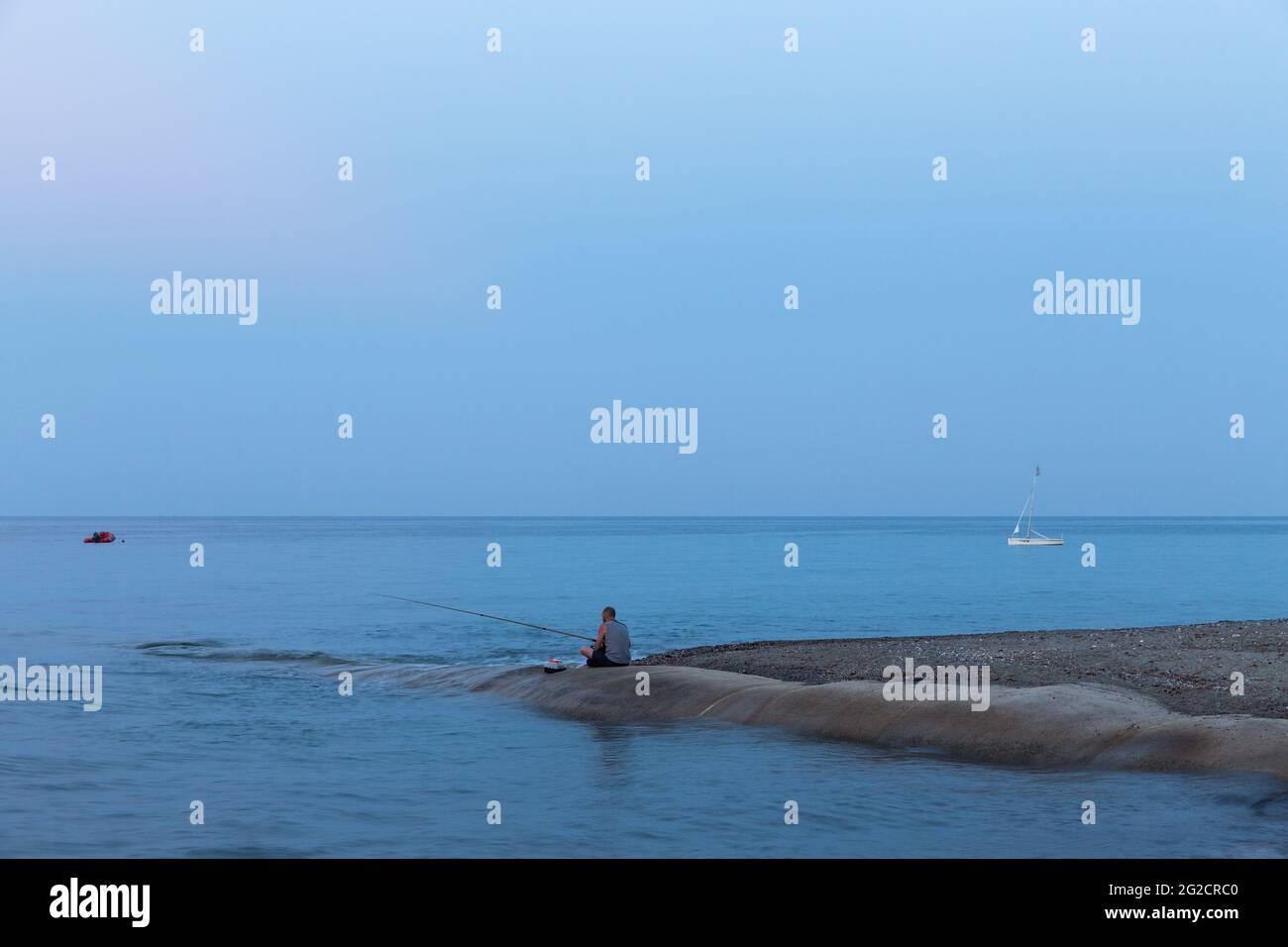 Pescador sentado al lado del mar al anochecer. Moriani-Plage, Córcega. Francia Foto de stock