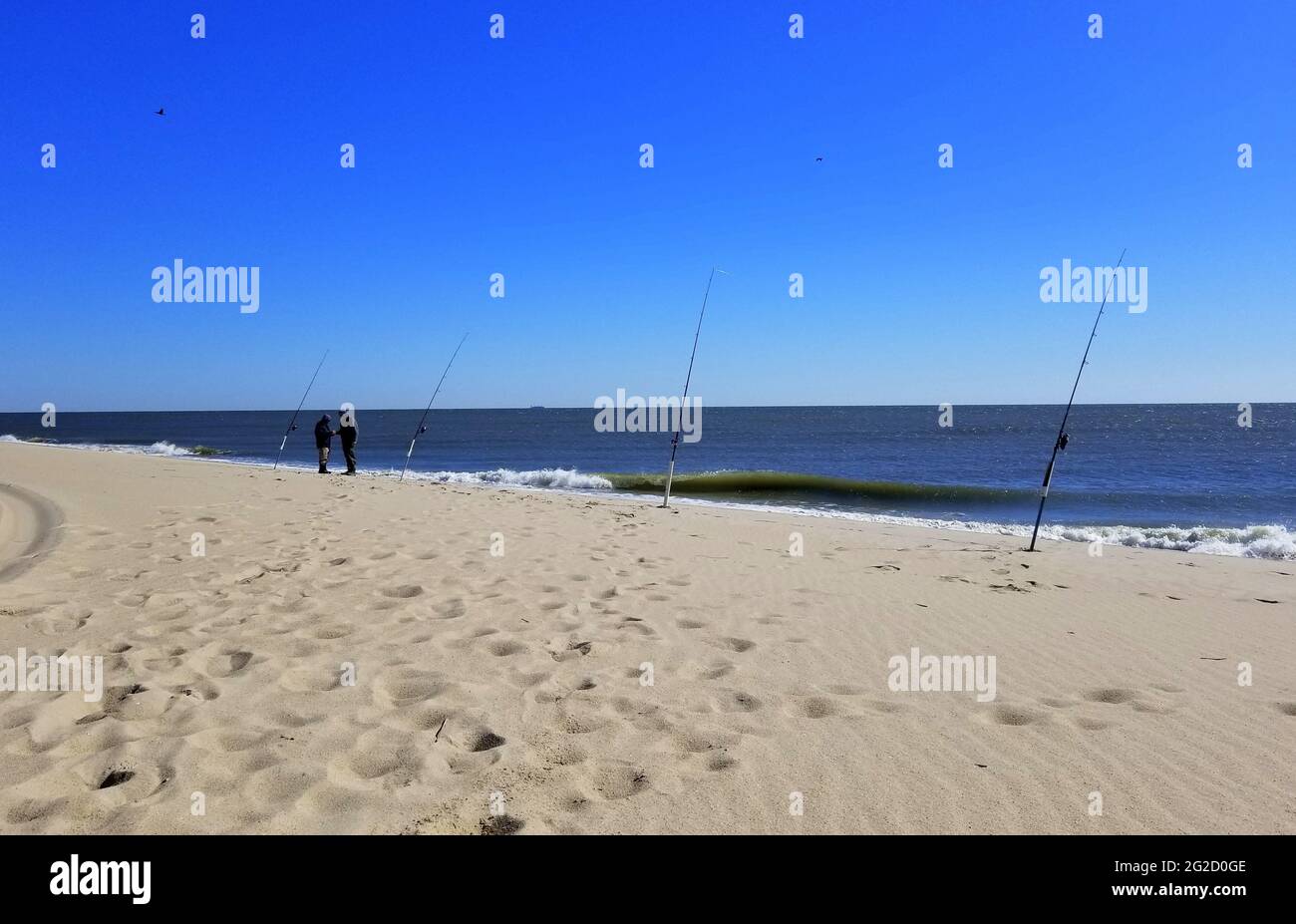 Playa de arena con cañas de pescar en un día soleado en la bahía de Delaware Foto de stock