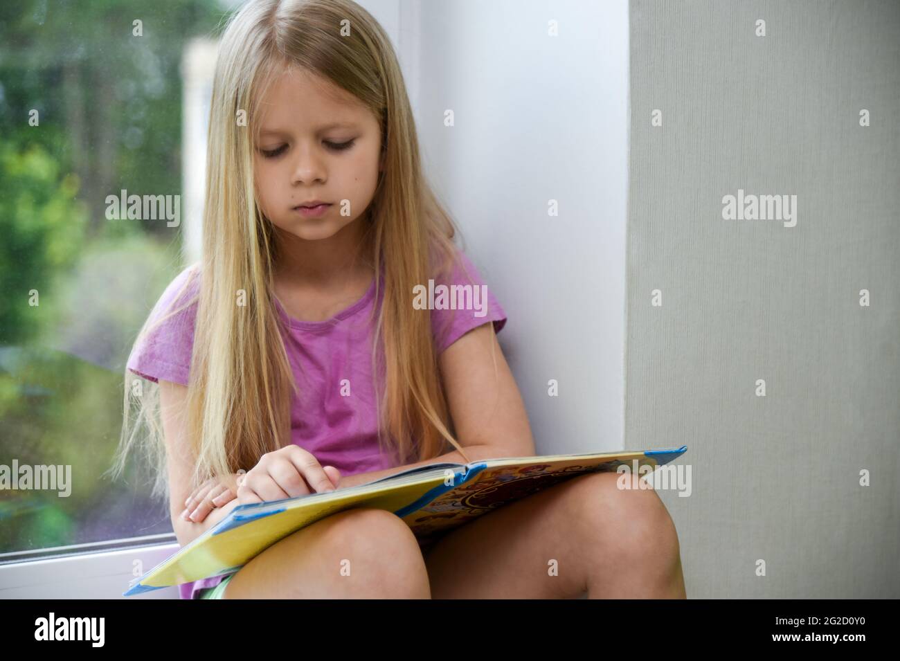 Niño leyendo un libro por la tarde en la ventana. Foto de stock