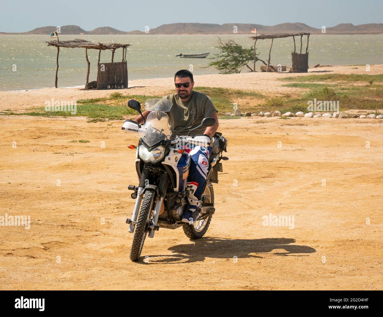 Bahia Honda, La Guajira, Colombia - 27 2021 de mayo: El hombre latino que monta una motocicleta está estacionando en el desierto al lado del océano Foto de stock