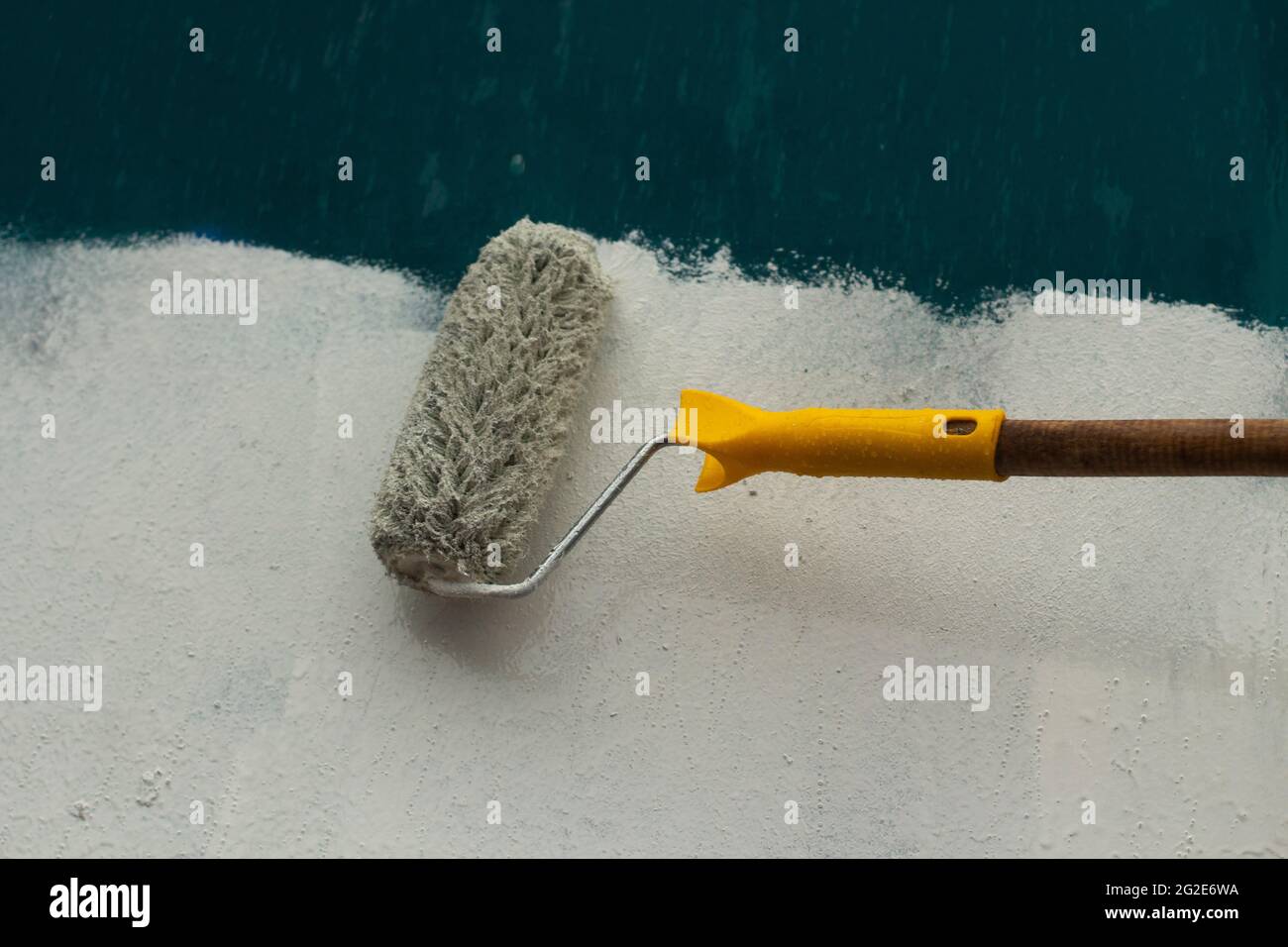 Un pintor pinta un muro de hormigón con pintura blanca, un macho de mano  con un rodillo de pintura para pintar una pared Fotografía de stock - Alamy