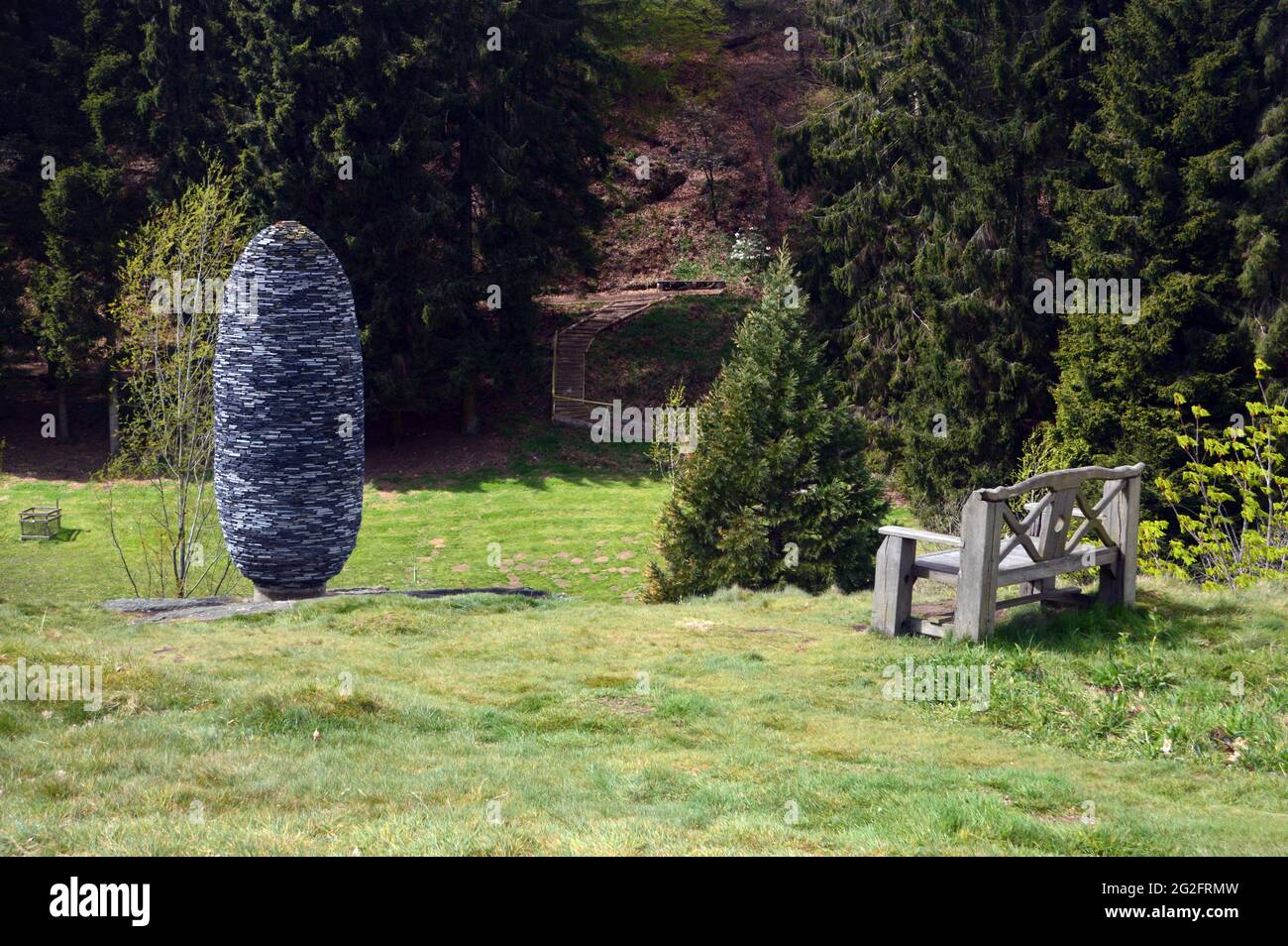 Banco de madera y la piedra 'cono de abeto' Escultura El Himalaya Garden & Sculpture Park, Grewelthorpe, Ripon, North Yorkshire. Foto de stock