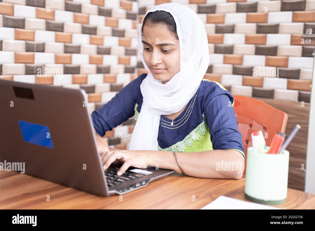 Joven india con la cabeza cubierta usando el portátil en el hogar - concepto de la educación en línea, el trabajo desde el hogar o la fmh, la tecnología y el estilo de vida Foto de stock