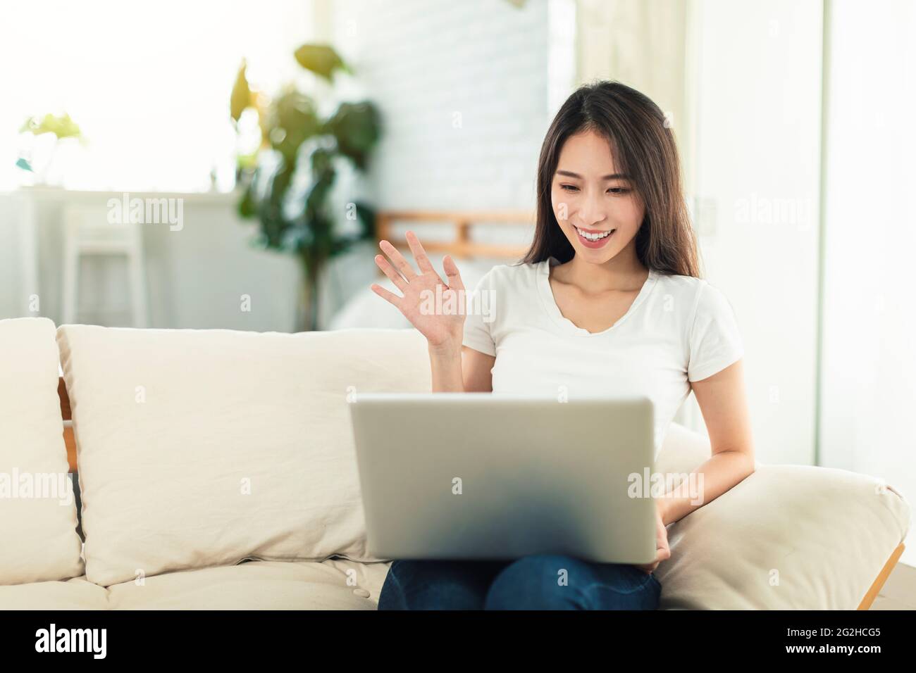 Mujeres jóvenes que trabajan desde casa, sentados en el sofá usando ordenadores portátiles para teletrabajo, y video chateando con colegas Foto de stock