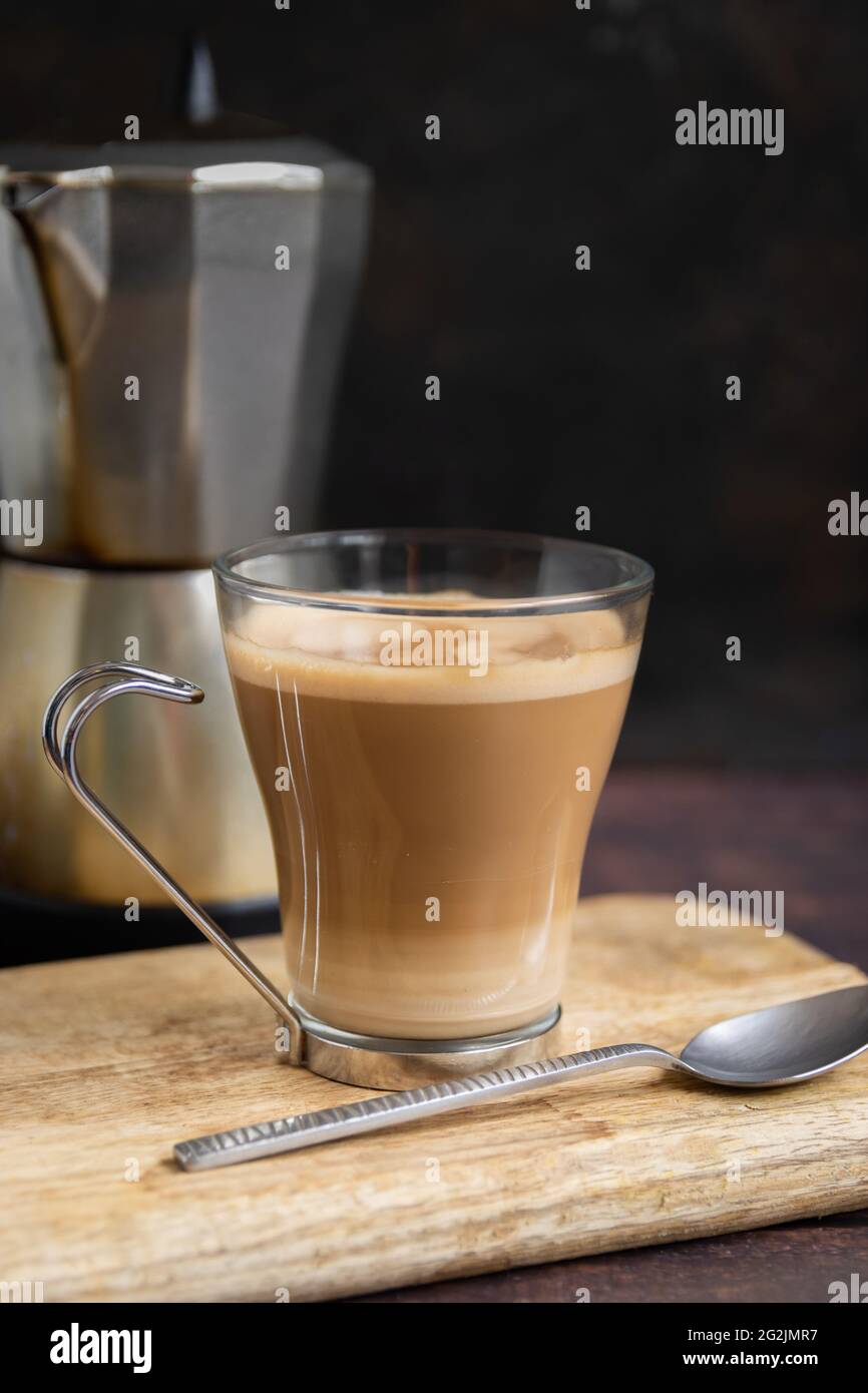 Taza de café con leche y cucharadita en mesa de madera y cafetera italiana  en el fondo. Vertical Fotografía de stock - Alamy