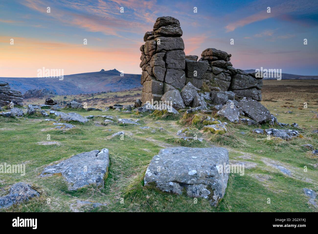 La fotografía presenta rocas en Hound Tor en el Parque Nacional Dartmoor en Devon capturadas al amanecer con Haytor en la distancia. Foto de stock