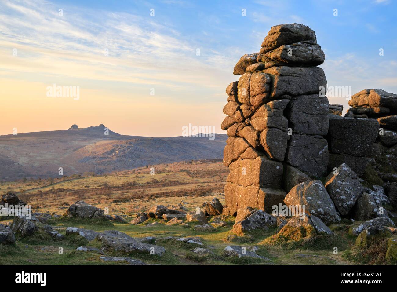 La fotografía presenta rocas en Hound Tor en el Parque Nacional de Dartmoor en Devon capturadas poco después del amanecer con Haytor en la distancia. Foto de stock