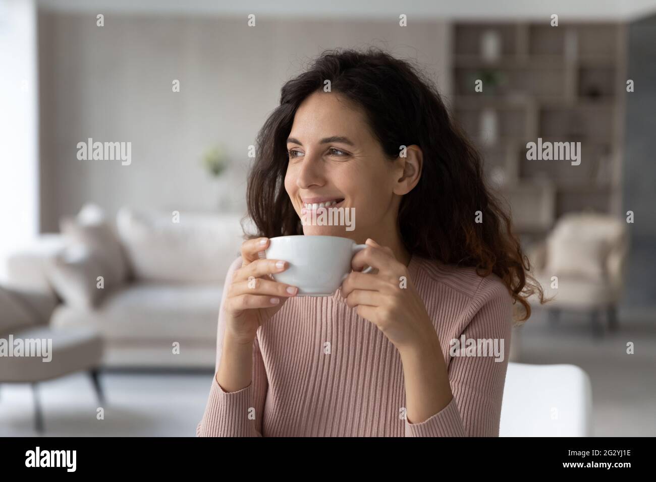 Una feliz mujer latina bebe café soñando en casa Foto de stock