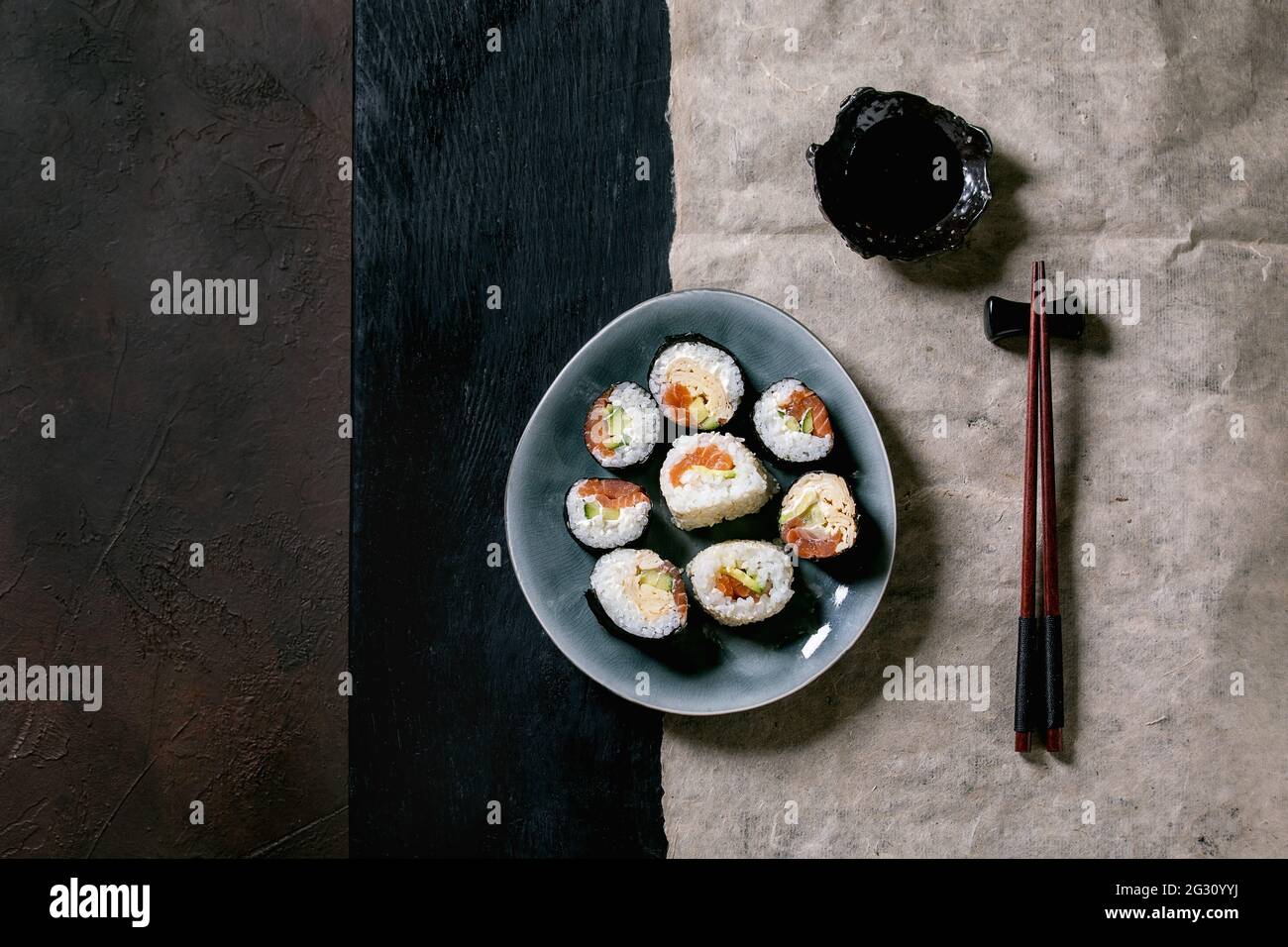 Rollos de sushi caseros con salmón, tortilla japonesa, avacado y salsa de soja con palillos de madera sobre fondo de textura oscura Vista superior, Foto de stock